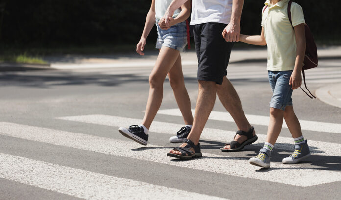 Family crossing street AdobeStock_267665355 Father holding hands with his kids while on pedestrian crossing