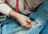Bringing the art of repair back to the community A woman mends jeans, sews a patch on a hole, hands close-up