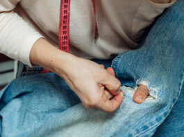 Bringing the art of repair back to the community A woman mends jeans, sews a patch on a hole, hands close-up